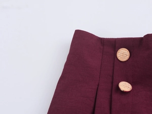 Close-up of burgundy straight-leg trousers with elegant gold textured buttons and fabric pleats