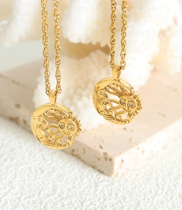 Detailed close-up of gold celestial sun and moon pendant necklaces on a stone surface
