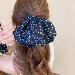 Close-up of a large navy floral bow hair clip worn on a low ponytail for a sweet style