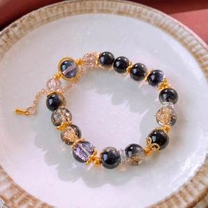 Macro detail of beaded bracelet with black stones and purple crystals on a ceramic dish