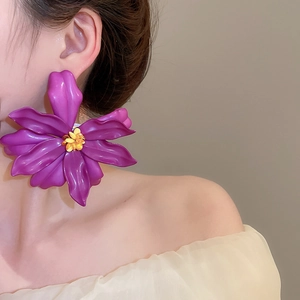 Close-up of oversized purple acrylic flower earrings with yellow beaded centers on a model