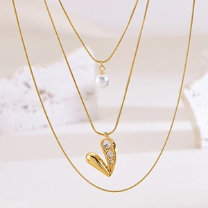 Layered gold chain necklace featuring a white pearl and a heart pendant with zircons
