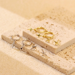 Detail of silver and gold star pendant earrings on beige stone texture surface