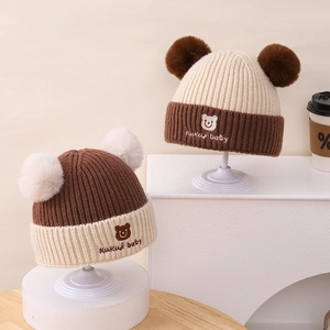 Detailansicht der gestrickten Baby-Mützen mit zwei Bommeln und süßer Bärenstickerei