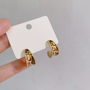 Close-up of vintage gold C-shaped enamel earrings with hollow pattern on card