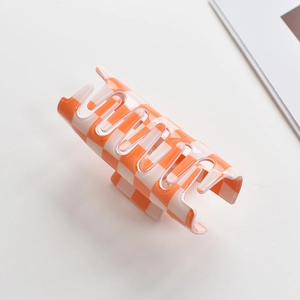 Close-up of orange and white checkerboard claw clip made of durable resin on a white desk
