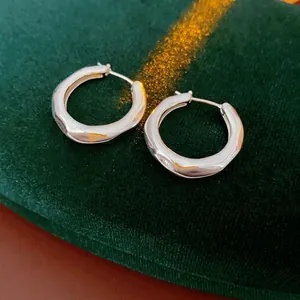 Polished silver irregular twisted hoop earrings displayed on green velvet with warm lighting