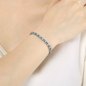 Detail of silver tennis bracelet with blue and white zircon stones on a female wrist