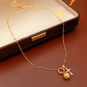 Dettaglio della collana con croce dorata, sfera cava e zircone su base in pelle