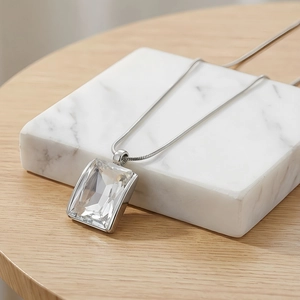 Macro view of clear rectangle crystal pendant on a silver snake chain over marble