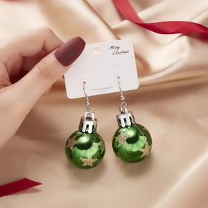 Detail of green Christmas bulb earrings with gold stars on elegant satin background