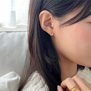 Close-up of minimalist golden bean earrings and stacked rings worn by a model