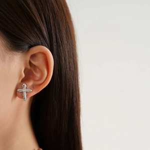 Macro detail of silver cross stud earring with ornate relief and small diamond