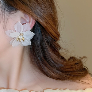 Detail shot of a matte white petal earring with a pearl center on a model's ear