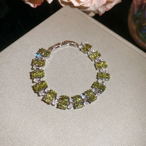 Detail of silver bracelet featuring olive green oval gemstones and white pave crystals