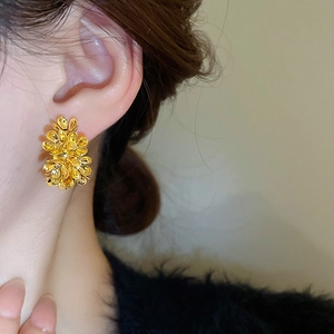 Close-up of model wearing gold metal flower C-shaped stud earrings with textured petals
