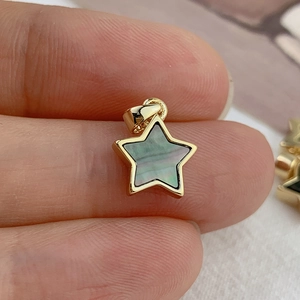 Pendentif étoile doré avec nacre noire incrustée tenu entre les doigts