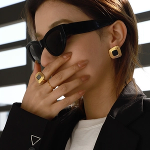 Detail of geometric gold earrings and matching black stone ring on model