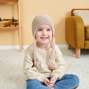 Detailed knit texture and cute braided earflaps on beige warm winter hat for kids