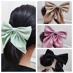 Detailed view of oversized satin bow hair clips in light green, beige, pink and black