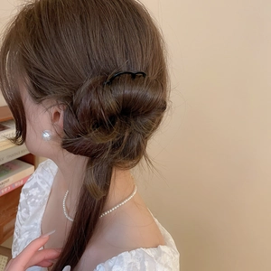 Gros plan d'une épingle à cheveux noire en U fixant un chignon bas élégant