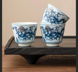 Detail of ceramic tea cups with blue dragon pattern and gold accents on a wooden tray