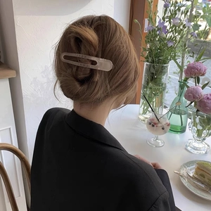 Matte beige rectangular hair claw clip worn by a model in a natural cafe setting