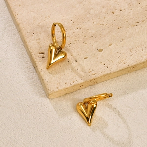Detailed macro view of heart-shaped gold dangling earrings on a textured stone surface