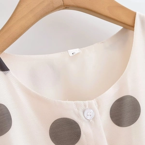 Gros plan sur la robe beige à pois avec col rond, boutons et texture du tissu