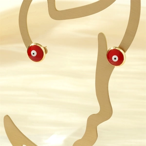 Macro detail of red evil eye stud earrings on gold metal mannequin with a fabric background