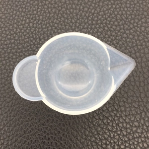 Close-up of a 100ml silicone measuring cup with scale and spout on a dark textured background