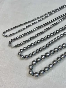 Detail showing five different sizes of dark grey pearl necklaces on white linen texture