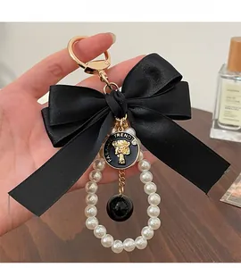 Close-up of black satin bow keychain with white pearls and golden medallion detail