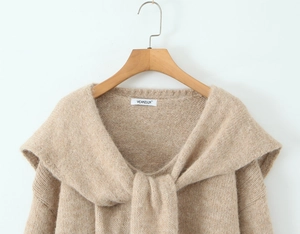 Detailed view of beige knit sweater with large lapel collar on a wooden hanger