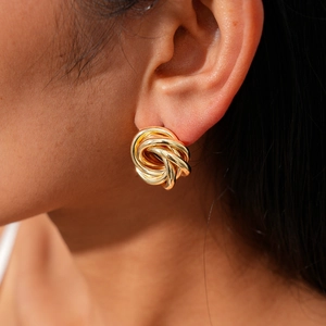 Close-up of model wearing gold twisted knot stud earrings with a polished metal finish
