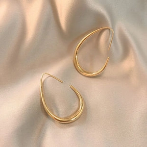 Macro detail of gold-plated teardrop earrings on elegant champagne satin fabric background