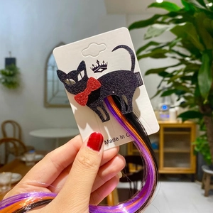 Close-up of glittery black cat hair clip with red bow and colorful Halloween extensions