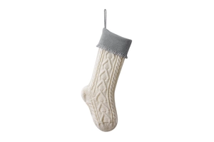 Close-up of cable knit Christmas stocking with gray cuff and tassel detail on white background