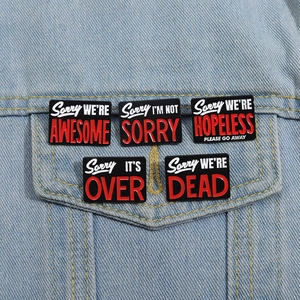 Detail of five black enamel pins with motivational quotes pinned on a denim jacket pocket