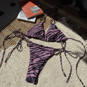 Detailed shot of pink zebra print bikini with gold teardrop metal rings on straw rug