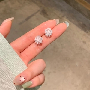 Detailed close-up of white crystal flower cluster earrings on a finger