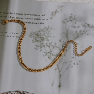 Flat gold curb chain necklace with lobster clasp and K18 tag on aesthetic paper background