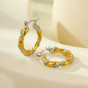 Macro detail of twisted C-shape hoop earrings featuring gold and silver weaving texture