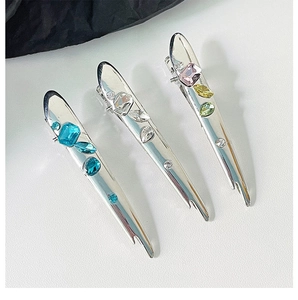Detail of liquid metal hair clips with blue, clear and multicolor crystals on white surface