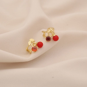 Close-up of cherry-shaped earrings with red zircon and gold-tone base on soft beige fabric