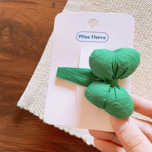 Detail of a green fabric bow hair clip displayed on a white brand card for girls