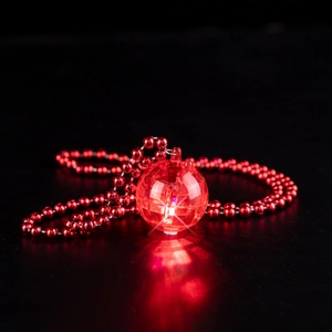 Macro shot of 1970s retro disco ball pendant glowing in red light on a beaded chain