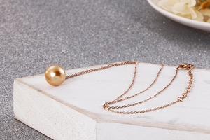 Détail d'un collier pendentif en perle avec chaîne en or rose sur socle en bois blanc