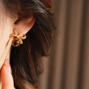 Detail of golden bow earrings with zircon and brown bead worn by a model