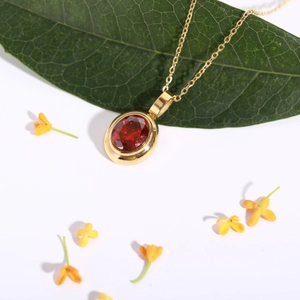 Detail of 18k gold plated necklace with oval red gemstone pendant on a green leaf